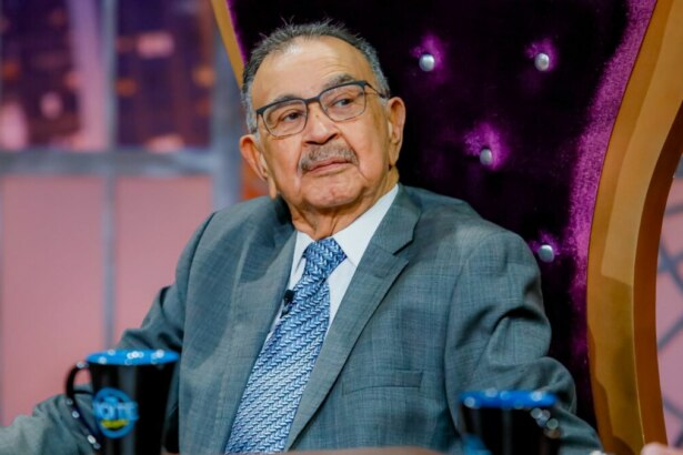 Percival de Souza, de terno e gravata, sentado em um trono, no programa The Noite