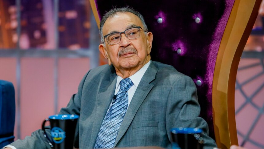 Percival de Souza, de terno e gravata, sentado em um trono, no programa The Noite