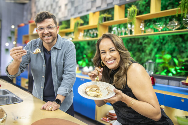 Guga Rocha com a boca aberta e segurando um talher com Tiramisu. Ele está ao lado de Renata Alves que segura o prato com a receita na cozinha do Hoje em Dia