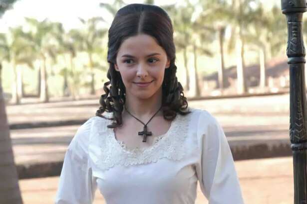 Bianca Rinaldi de vestido branco e com um colar de cruz no pescoço em campo nos bastidores de A Escrava Isaura