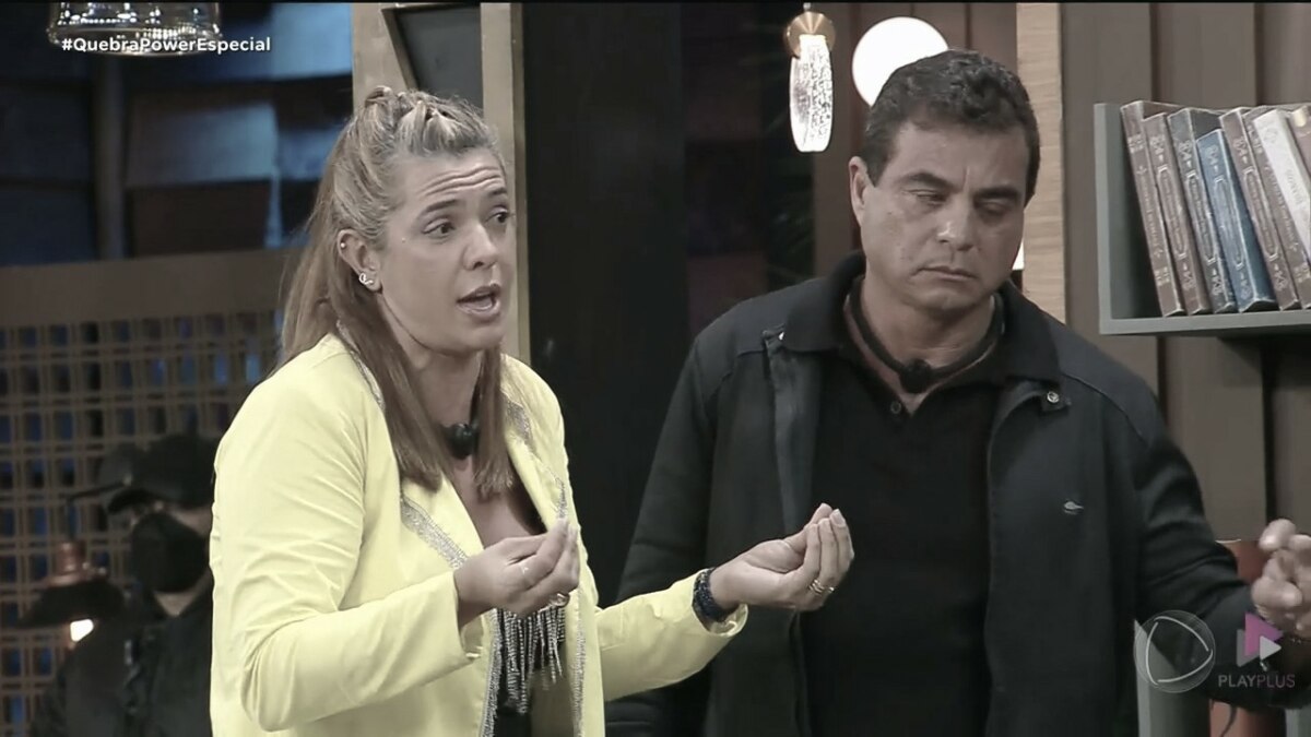 Adriana ao lado de Dhomini gesticulando, nervosa, tentando explicar a mentira no Power Couple Brasil 7