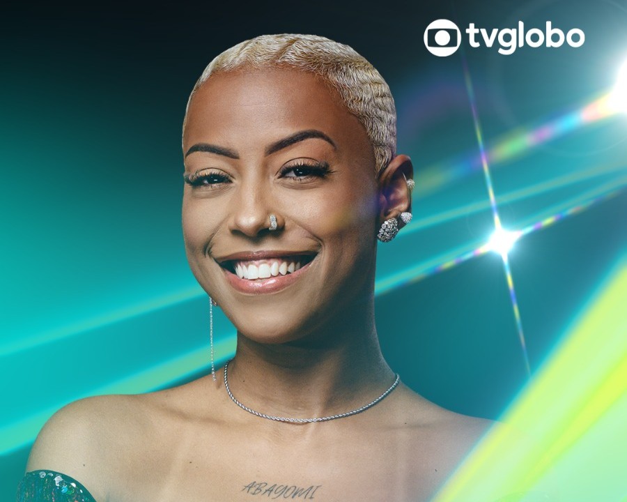 Bea é uma mulher negra, cabelo curto, platinado. Ela tem um piercing no nariz e e está sorridente