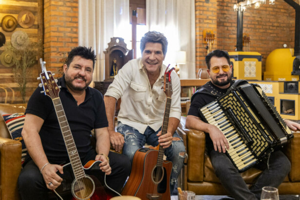 Bruno e Marrone sentados no sofá segurando guitarra e sanfona. Por trás deles o apresentador Daniel nos bastidores do Viver Sertanejo