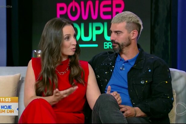 Carol e Radamés sentados no sofá do Hoje em Dia. Carol veste um vestido vermelho e Radamés de jaqueta preta e camisa azul