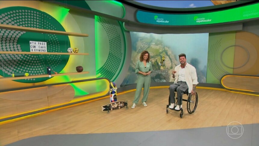 Karine Alves em pé e Fernando Fernandes sentado em sua cadeira de rodas no cenário do Esporte Spectacular