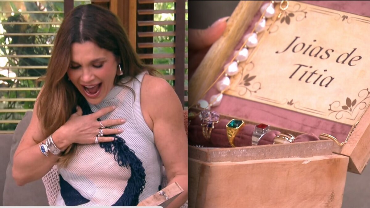 Flávia Alessandra abre caixa com as joias de titia e dá um grito com a mão no peito. A atriz está sentada no sofá do É de Casa