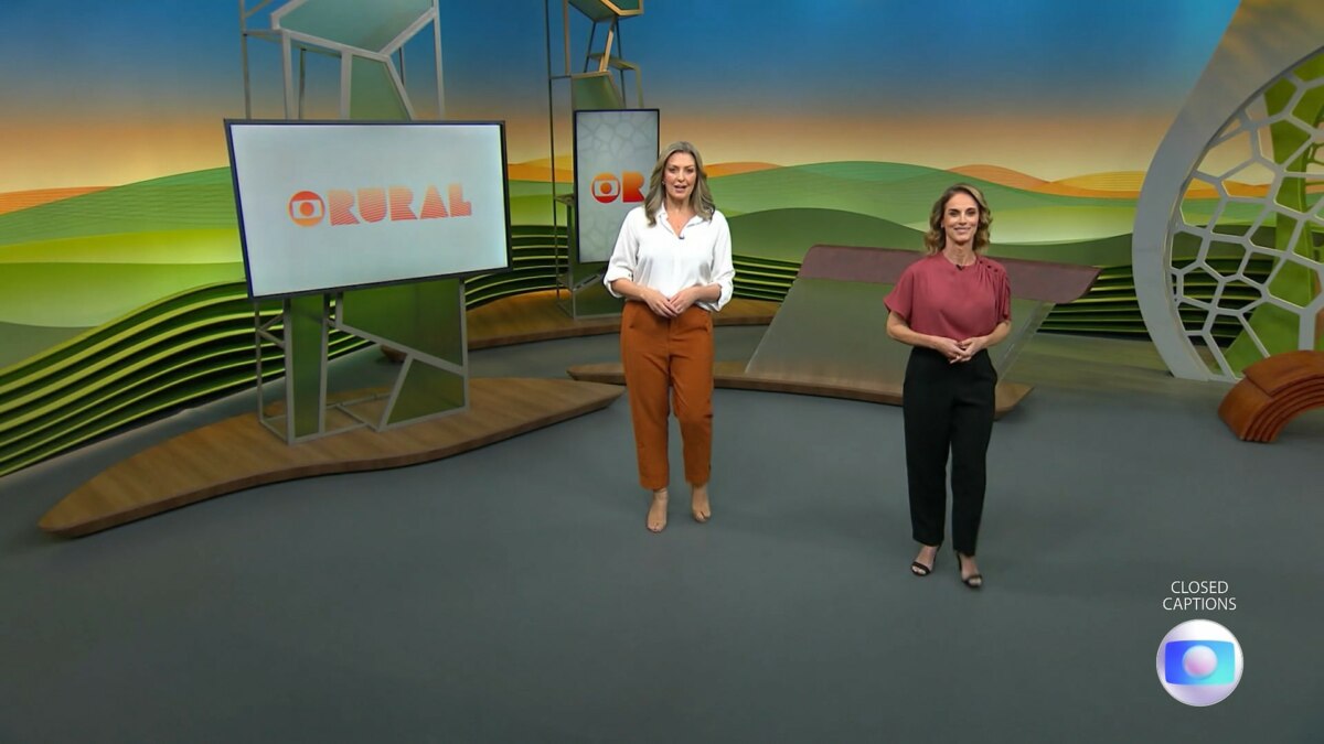 Cristina Vieira e Helen Martins caminha pelo cenário do Globo Rural na abertura do programa. Elas estão sorridentes. Cristina veste branco e marrom. Helen veste um conjunto rosa e preto