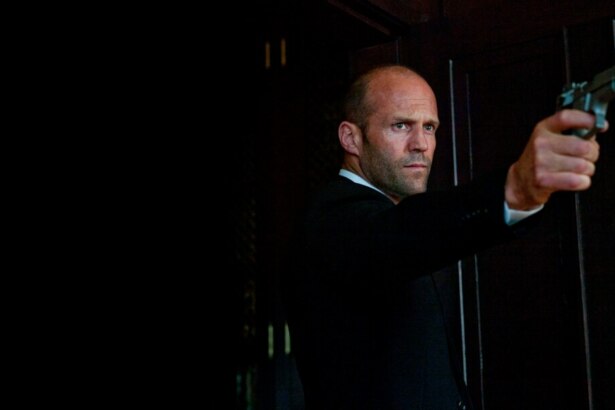 Jason Statham aponta uma arma na gravação do filme Parker