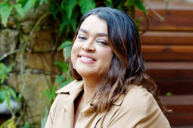 Preta Gil com blusa marrom e sorridente. Ela está sentada em um jardim