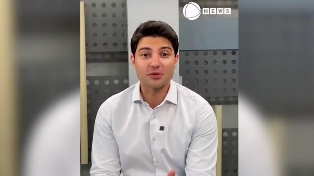 Rafael Algarte de camisa branca no cenário da Record News. O apresentador está sorridente
