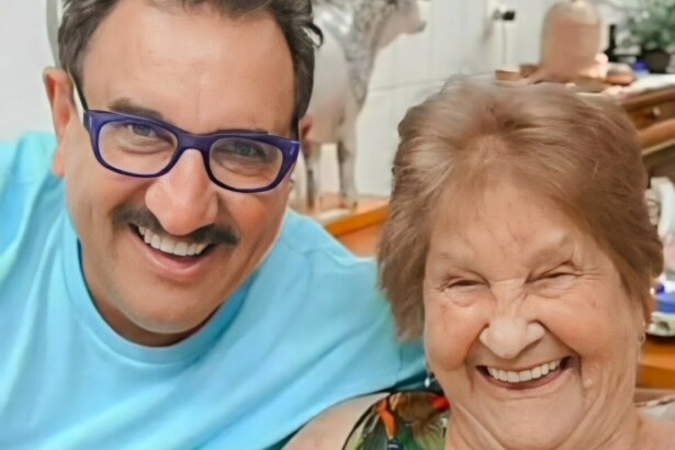 Ratinho sorridente ao lado de sua Maria Massa que está sentada em uma cadeira. Os dois estão sorrindo