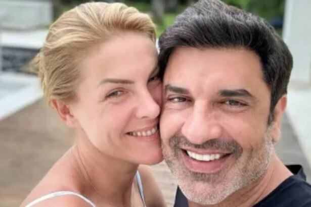 Uma foto de perto de Ana Hickmann e Edu Guedes. Ana, à esquerda, é uma mulher de pele clara com cabelos loiros presos, sorrindo e com a cabeça inclinada para perto de Edu. Edu, à direita, é um homem de pele clara com cabelos escuros e barba por fazer, sorrindo amplamente para a câmera. Ambos parecem estar ao ar livre, com um fundo desfocado.