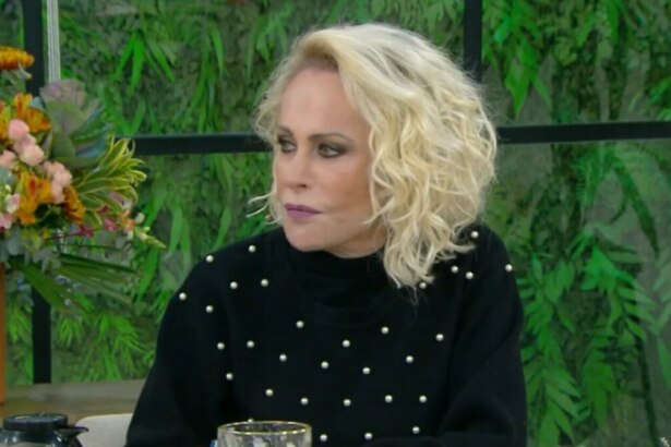 A apresentadora Ana Maria Braga, com um olhar sério, sentada em uma bancada de estúdio de televisão. Ela usa um suéter preto de gola alta com pequenos detalhes brancos. Ao fundo, o cenário é de um ambiente interno com plantas e janelas.