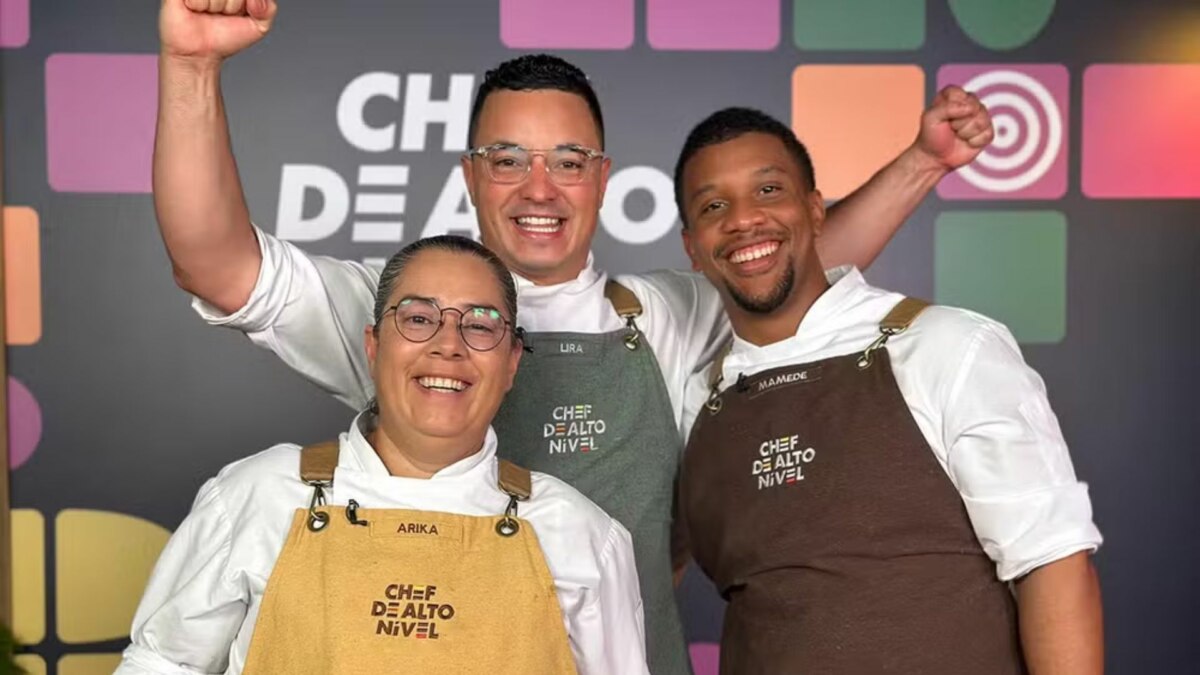 A imagem mostra três finalistas do reality show "Chef de Alto Nível". Da esquerda para a direita, Arika, Lira e Mamede. Os três estão sorrindo e comemorando, com os punhos erguidos. Todos vestem dólmãs brancos e aventais de chef com a inscrição "CHEF DE ALTO NÍVEL". O painel ao fundo repete o nome do programa.