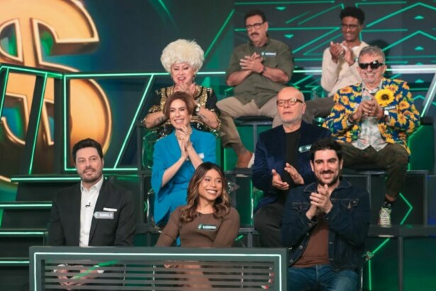 Uma bancada de celebridades em um estúdio de televisão do programa "Show do Milhão". Há nove pessoas, homens e mulheres, sentadas em cadeiras em diferentes níveis. O cenário tem um grande cifrão dourado e luzes verdes. Na primeira fila, o apresentador Danilo Gentili e a apresentadora Blogueirinha, de casaco azul, estão visíveis.