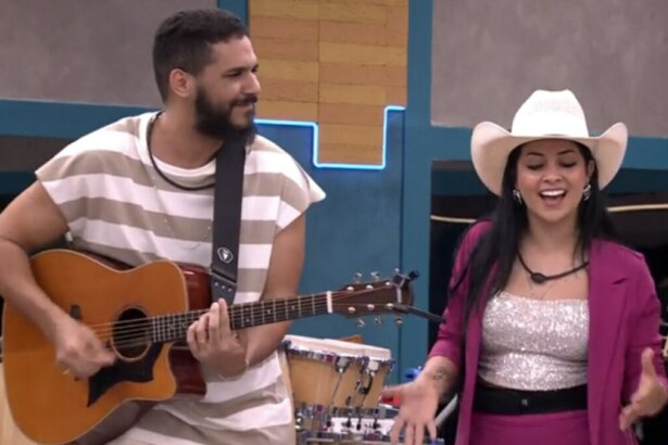 Brenno Casagrande e Biahh Cavalcante no reality Estrela da Casa. Ele toca violão e sorri para ela, que canta usando um chapéu de cowboy e um blazer rosa.