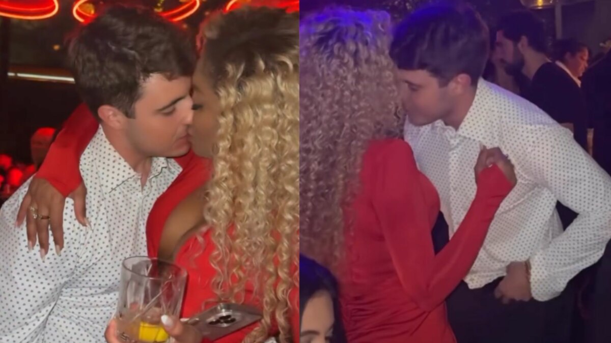 A imagem é uma montagem de duas fotos. À esquerda, a apresentadora Cariúcha, com cabelos loiros e cacheados e um vestido vermelho, e João Augusto Liberato, com uma camisa social branca de bolinhas, estão se beijando. Cariúcha segura um copo de bebida e tem um de seus braços ao redor do pescoço de João Augusto. À direita, eles se beijam novamente, de um ângulo diferente. O ambiente é um local com pouca iluminação, com pessoas ao fundo.