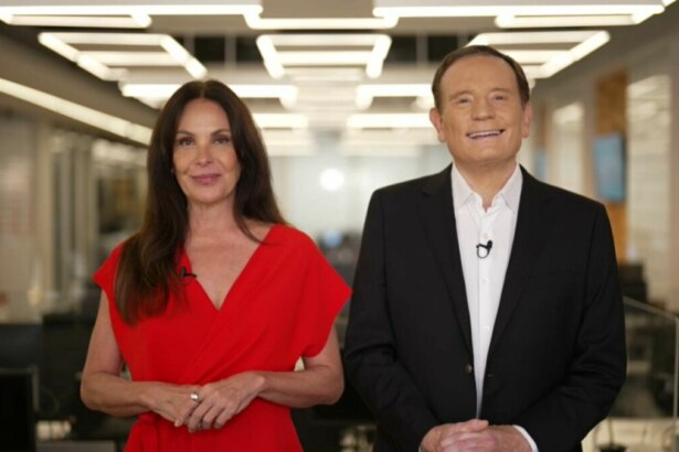 A apresentadora Carolina Ferraz, de vestido vermelho, e o jornalista Roberto Cabrini, de terno preto, estão em um estúdio. Ambos sorriem para a câmera, e o nome do arquivo os associa ao programa 'Domingo Espetacular'.