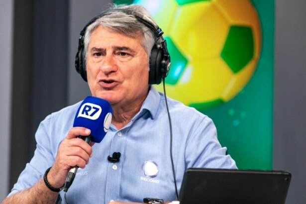O narrador Cléber Machado em um estúdio da Record. Ele usa fone de ouvido e segura um microfone, falando durante uma transmissão esportiva.