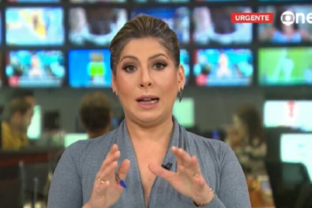 A jornalista Daniela Lima apresentando o jornal da GloboNews, em um estúdio de telejornalismo. Ela fala e gesticula com as mãos. Ao fundo, um painel de telas de TV exibe imagens e o logo da emissora com o aviso "URGENTE". Também é possível ver a redação do canal desfocada.