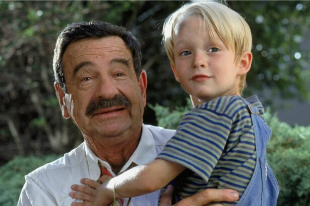 O garoto Dennis Mitchell é segurado pelo seu vizinho, Sr. Wilson, que tem um bigode e usa camisa e gravata, em cena do filme Dennis, o Pimentinha