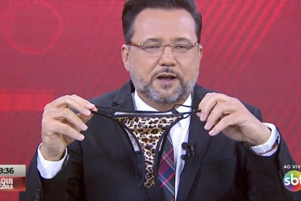 O apresentador Geraldo Luís, usando terno e gravata, segura com as duas mãos uma calcinha de estampa de onça. Ele está no estúdio do programa "Aqui Agora", da emissora SBT, cujo logo e o do programa são visíveis no canto inferior da tela. O fundo é um painel vermelho.