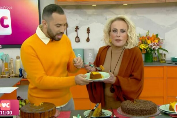 Gil do Vigor e Ana Maria Braga no programa "Mais Você". Ana Maria oferece um pedaço de bolo de cenoura a Gil do Vigor em um prato. Ambos sorriem, e na bancada em frente a eles, há outros bolos. O cenário é a cozinha do estúdio.