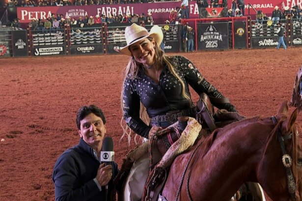 Um repórter de terno escuro, segurando um microfone com o logo da Globo, sorri para a câmera. Ao lado dele, uma mulher de chapéu de caubói e camisa preta bordada, sentada em um cavalo, também sorri. O fundo é uma arena de rodeio com público e banners no Globo Repórter