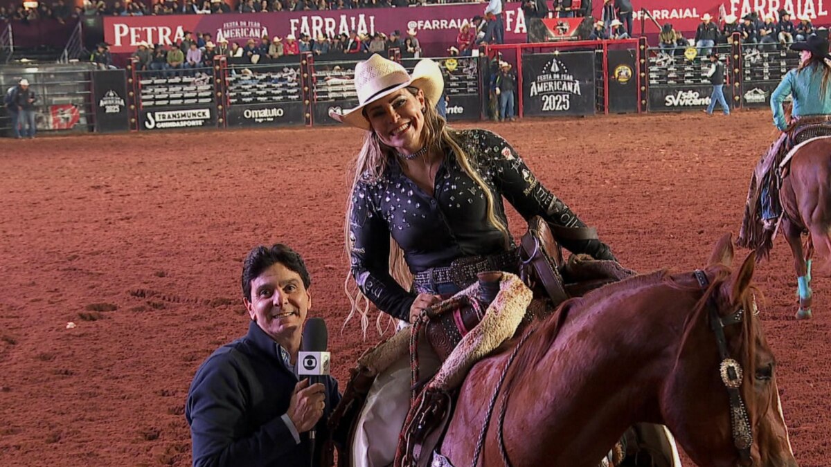 Um repórter de terno escuro, segurando um microfone com o logo da Globo, sorri para a câmera. Ao lado dele, uma mulher de chapéu de caubói e camisa preta bordada, sentada em um cavalo, também sorri. O fundo é uma arena de rodeio com público e banners no Globo Repórter