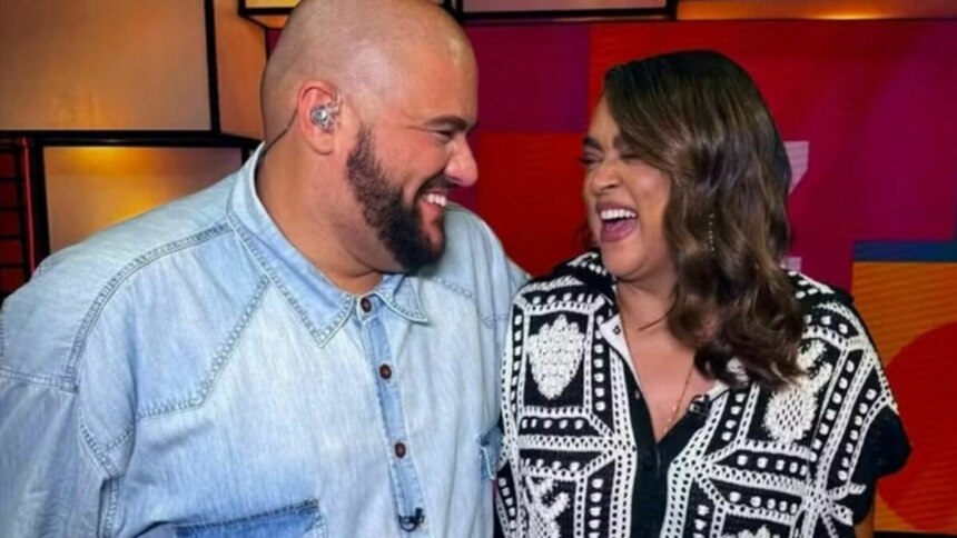 Gominho, careca e com barba, usando uma camisa jeans, e Preta Gil, com cabelos longos e ondulados e uma blusa preta e branca estampada, sorrindo e se olhando com alegria. Eles parecem estar em um ambiente de estúdio, com cores vibrantes ao fundo.