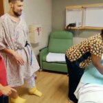 J.T. em um quarto de hospital, sendo acompanhado por duas profissionais de saúde, uma arrumando a cama e a outra observando