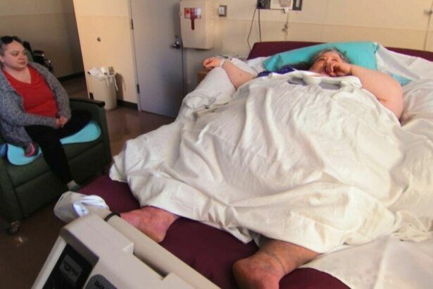 A participante Joyce, do programa Quilos Mortais, deitada em uma cama de hospital, enquanto outra mulher senta ao lado, observando-a com preocupação.