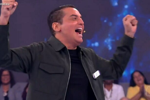 O apresentador Leo Dias, com uma jaqueta verde-escura, celebra com os punhos para o ar em um estúdio do Acerte ou Caia. Ele está sorrindo.