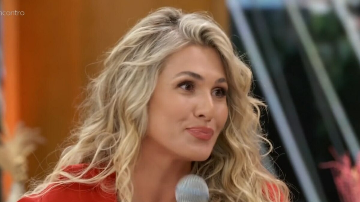 A apresentadora Lívia Andrade, de cabelos loiros e jaqueta vermelha, sorri em um close-up no programa 'Encontro'.