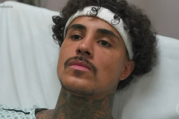 MC Livinho, homem com cabelos cacheados escuros e uma faixa branca na cabeça, deitado em uma cama de hospital, vestindo um avental hospitalar estampado. Ele tem barba e bigode finos, várias tatuagens visíveis no pescoço e olha para a frente com uma expressão séria. No canto superior esquerdo, há a hashtag "#Fantástico".