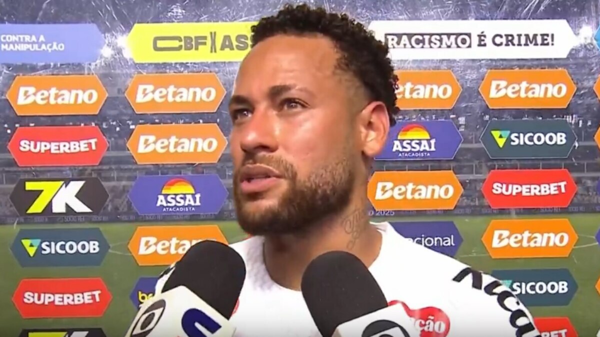 O jogador de futebol Neymar Jr., usando uma camisa branca, concede uma entrevista com expressão séria em frente a um painel de patrocinadores e fala sobre a Seleção Brasileira