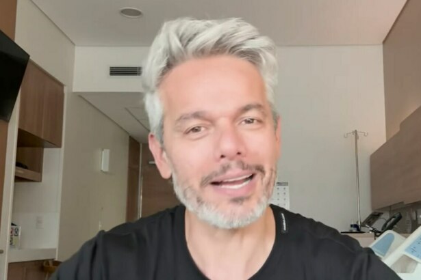 Otaviano Costa, com cabelo grisalho e barba, sorri em um quarto de hospital, após ser afastado do Melhor da Noite