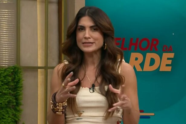 A imagem é um close da apresentadora Pâmela Lucciola, em uma cena do programa "Melhor da Tarde". Ela está em pé, gesticulando com as mãos enquanto fala. Pâmela usa uma blusa de alças bege com detalhes e braceletes e anéis dourados. Ao fundo, um painel com a inscrição "MELHOR DA TARDE" e o logo do programa.