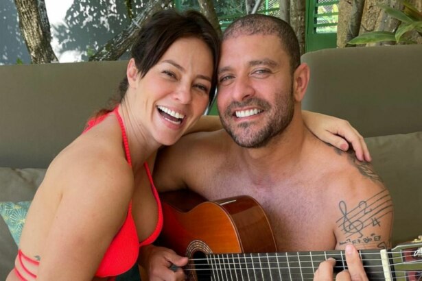 A atriz Paolla Oliveira e o cantor Diogo Nogueira posam para uma foto em um cenário natural. Paolla, de biquíni rosa, sorri para a câmera. Diogo, sem camisa, abraça Paolla enquanto toca um violão. Ele tem uma tatuagem de notas musicais no braço.