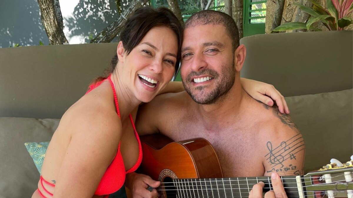 A atriz Paolla Oliveira e o cantor Diogo Nogueira posam para uma foto em um cenário natural. Paolla, de biquíni rosa, sorri para a câmera. Diogo, sem camisa, abraça Paolla enquanto toca um violão. Ele tem uma tatuagem de notas musicais no braço.