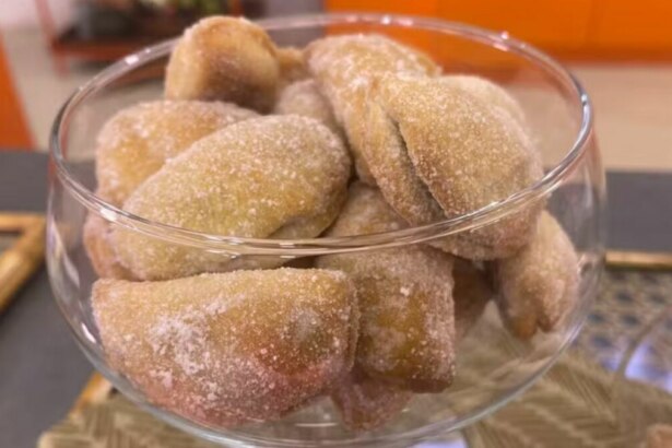 Um close-up de uma taça de vidro cheia de pastéis de nozes. Os pastéis são pequenos, ovais e polvilhados com açúcar. A imagem, com o nome do arquivo, é de uma receita do programa 'Mais Você'.