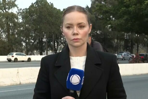 A repórter Beatriz Casadei, de casaco preto, está no acostamento de uma estrada. Ela segura um microfone com a logo da RECORD, e uma expressão séria.
