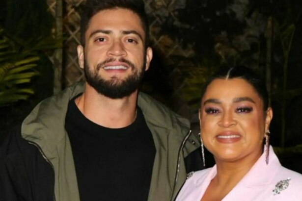 Rodrigo Godoy e Preta Gil posam sorridentes para a foto; ele veste jaqueta verde sobre camiseta preta, e ela usa blazer rosa claro com maquiagem em tons de rosa e brincos longos, em ambiente externo com plantas ao fundo.