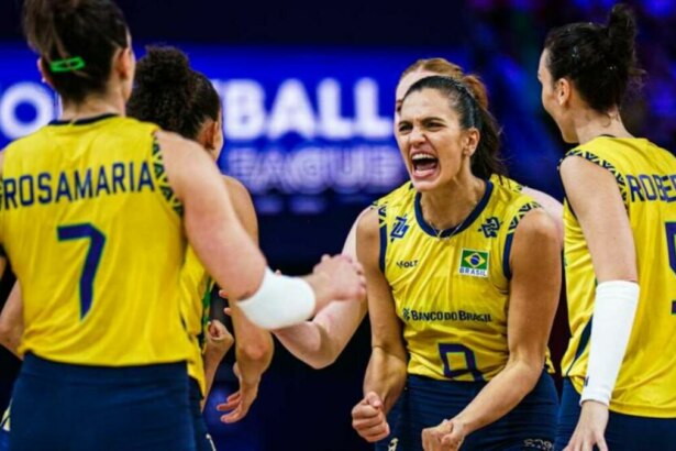 A imagem mostra a jogadora de vôlei Gabi Guimarães, com uma expressão de comemoração, em meio às suas colegas de equipe da Seleção Brasileira. Gabi está vestindo a camisa amarela com detalhes azuis. Ao fundo, uma placa com a inscrição "VOLLEYBALL LEAGUE". As jogadoras Rosamaria e Roberta, com as camisas 7 e 9, respectivamente, também são visíveis na imagem.