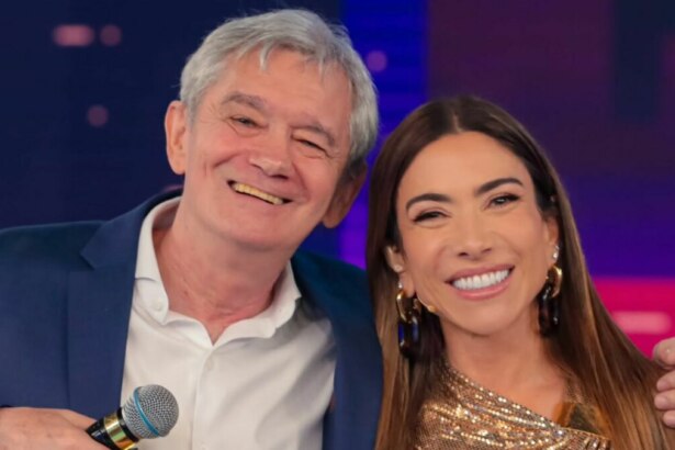Os apresentadores Serginho Groisman e Patricia Abravanel sorriem juntos para a câmera no estúdio do "Programa Silvio Santos". Serginho, de terno azul, pisca o olho e segura um microfone, enquanto Patricia, de top dourado, sorri largamente.