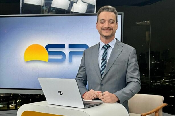 Tiago Scheuer sorridente em frente ao telão no cenário do Bom Dia SP