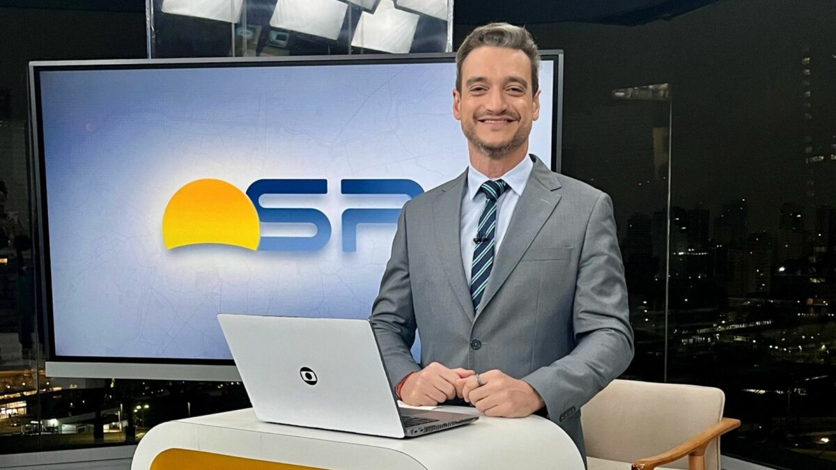 Tiago Scheuer sorridente em frente ao telão no cenário do Bom Dia SP