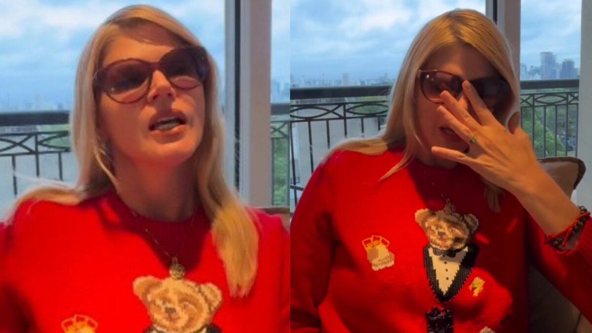 A imagem é uma montagem de duas fotos da socialite Val Marchiori. Nas duas fotos, ela está usando um suéter de lã vermelho com o desenho de um urso, e óculos de sol com armação marrom. Na foto da esquerda, ela está com a boca aberta, como se estivesse falando. Na foto da direita, ela aparece chorando, com a mão direita limpando as lágrimas. O fundo é uma janela com a vista de prédios.