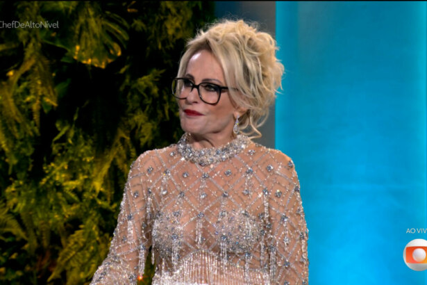 Ana Maria Braga na final do Chef de Alto Nível, vestindo um elegante vestido transparente com pedrarias brilhantes, penteado preso sofisticado e maquiagem marcante, em frente a um cenário com folhagens e iluminação azul, durante transmissão ao vivo da Globo