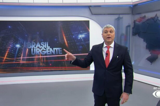 Joel Datena apresenta o Brasil Urgente em estúdio com visual urbano ao fundo e o logo do programa em destaque. A imagem representa a vitória do telejornal da Band na audiência, superando a estreia do Aqui Agora no SBT, mesmo com a presença de Geraldo Luís